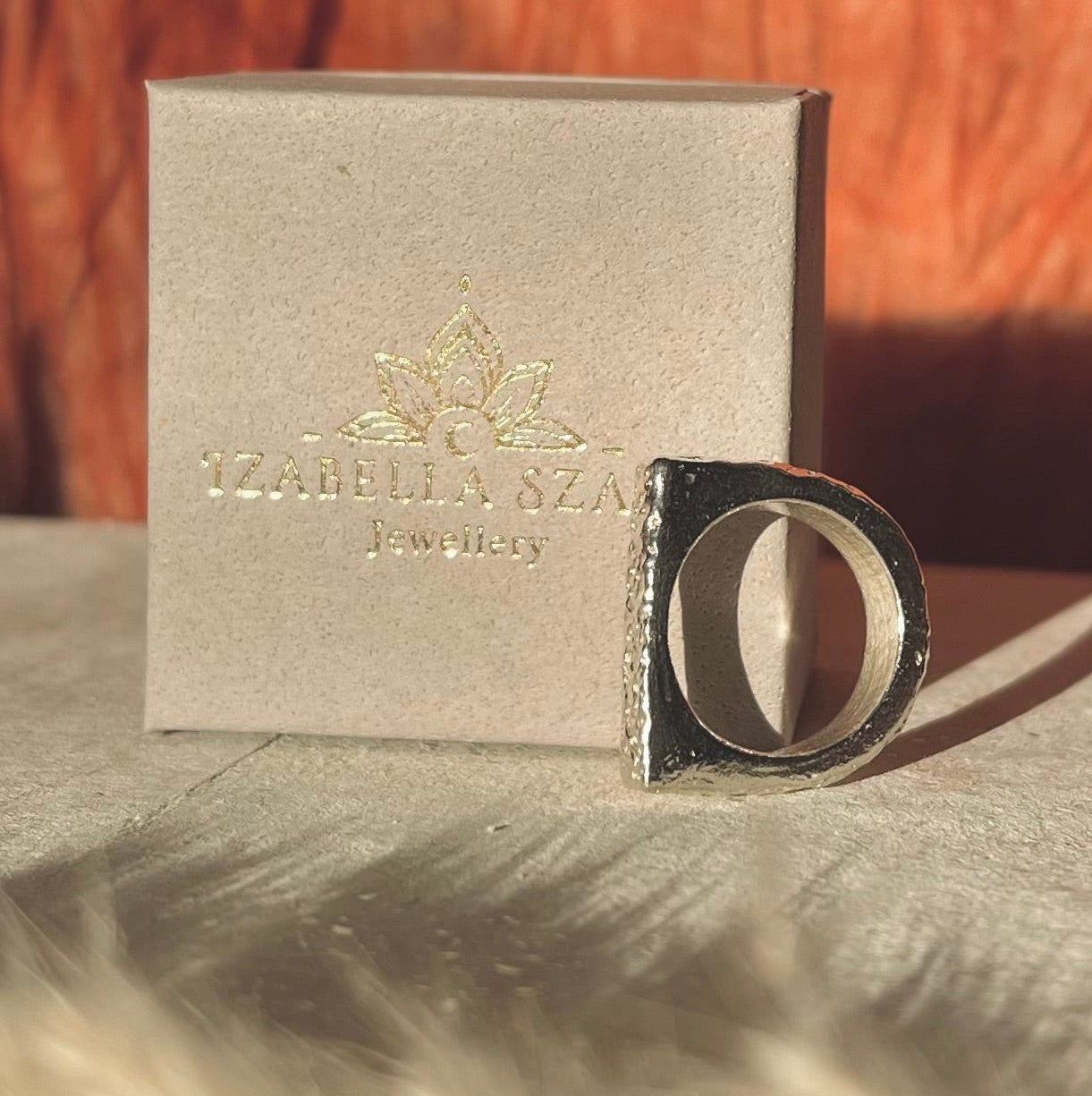 Silver ring with 'Yashika Ana' box on a textured surface