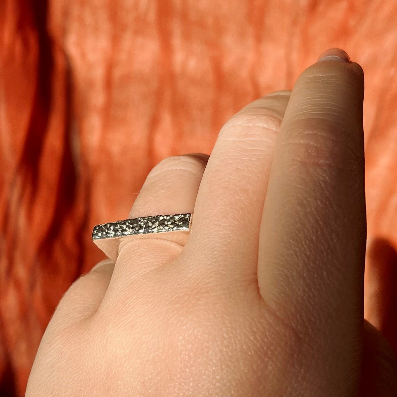Close-up of a hand wearing a silver ring with a textured band against a blurred background