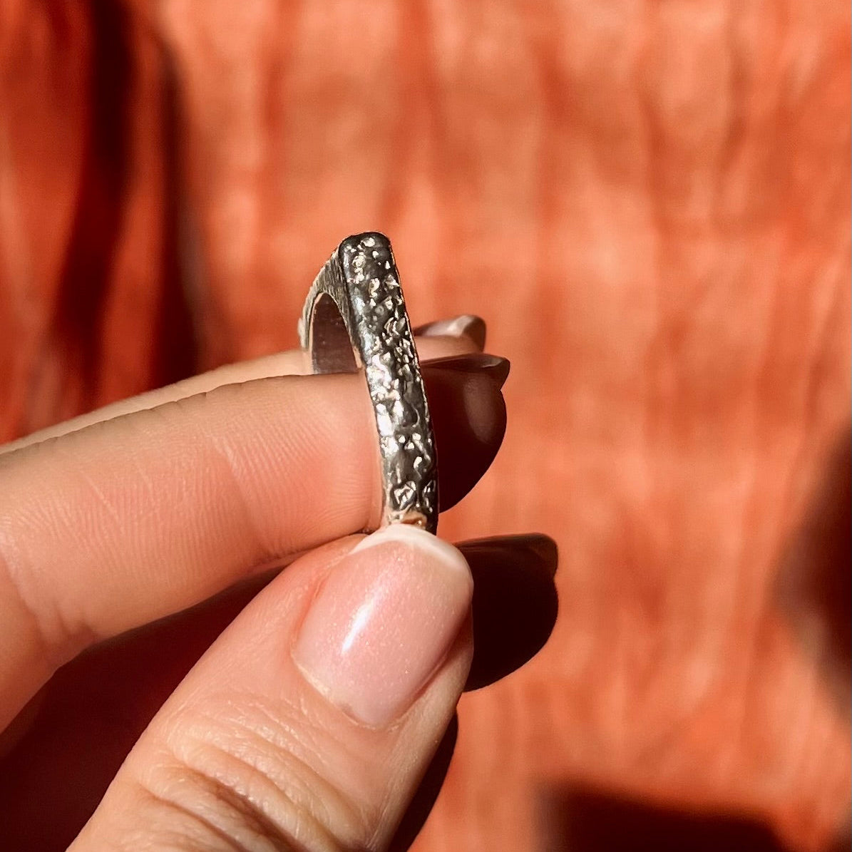 Silver ring held between fingers against a blurred background