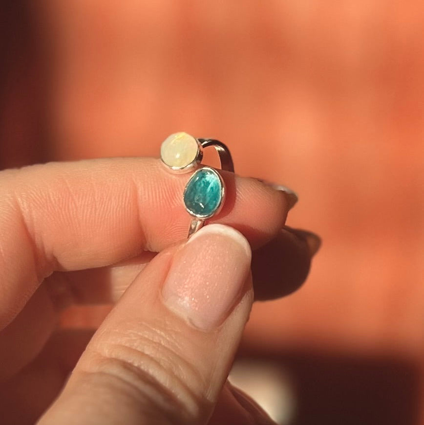 Ring with two stones held between fingers against a blurred background