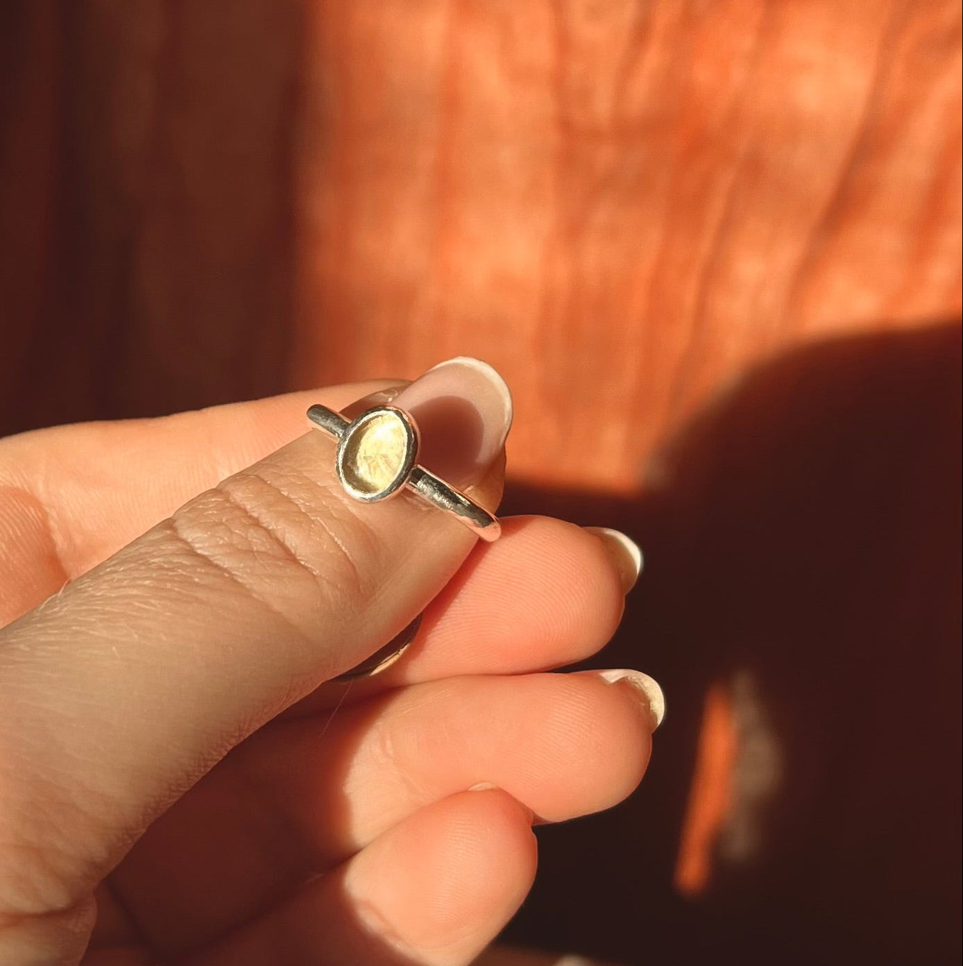Close-up of a hand holding a ring with a yellow gemstone against a blurred background