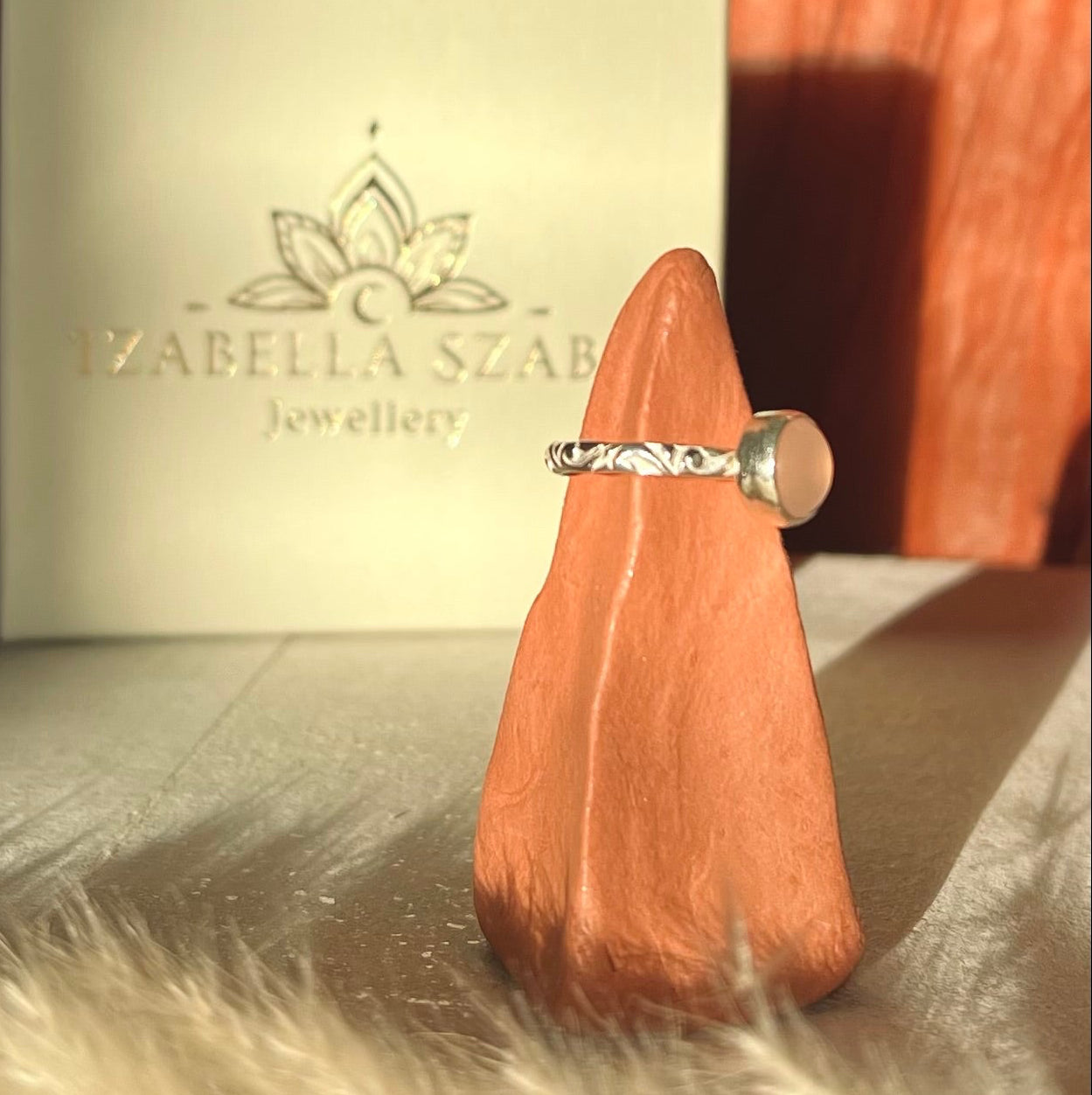 Silver ring on a wooden stand with a branded box in the background