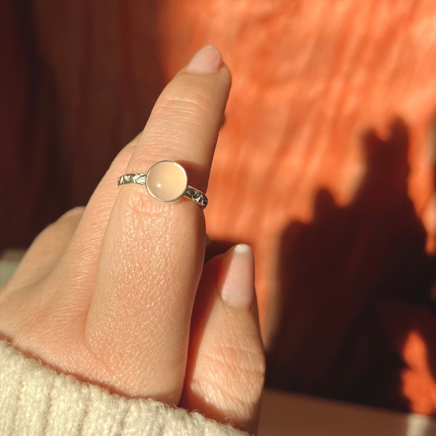 Close-up of a hand wearing a ring with a peach-colored gemstone against a blurred background