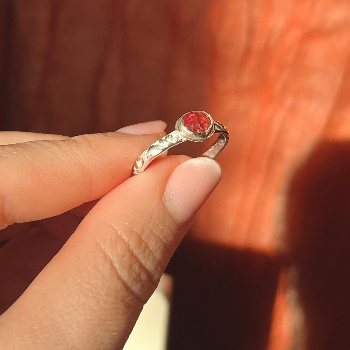 Hand holding a silver ring with a red stone against a wooden background