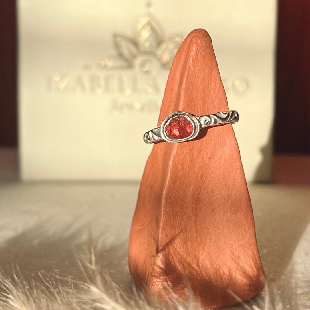 Silver ring with a red gemstone on a wooden block with a blurred background