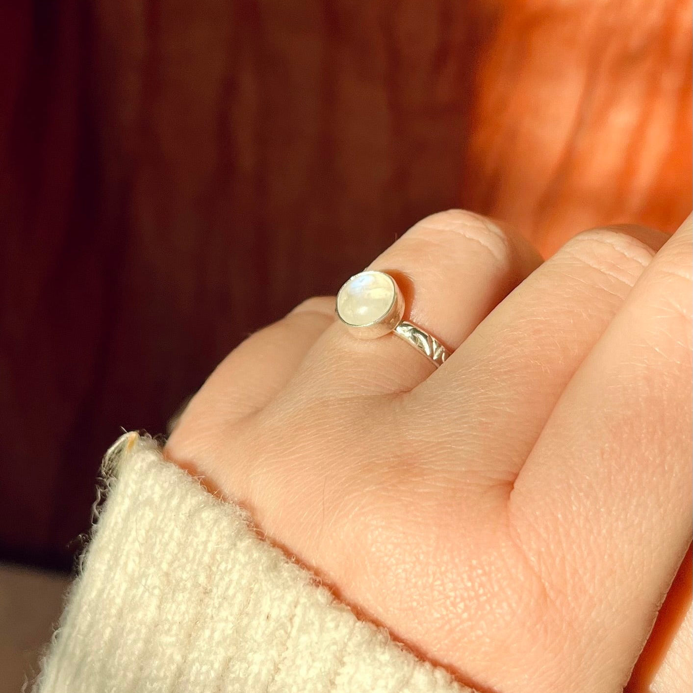 Close-up of a hand wearing a silver ring with a pearl on a blurred background