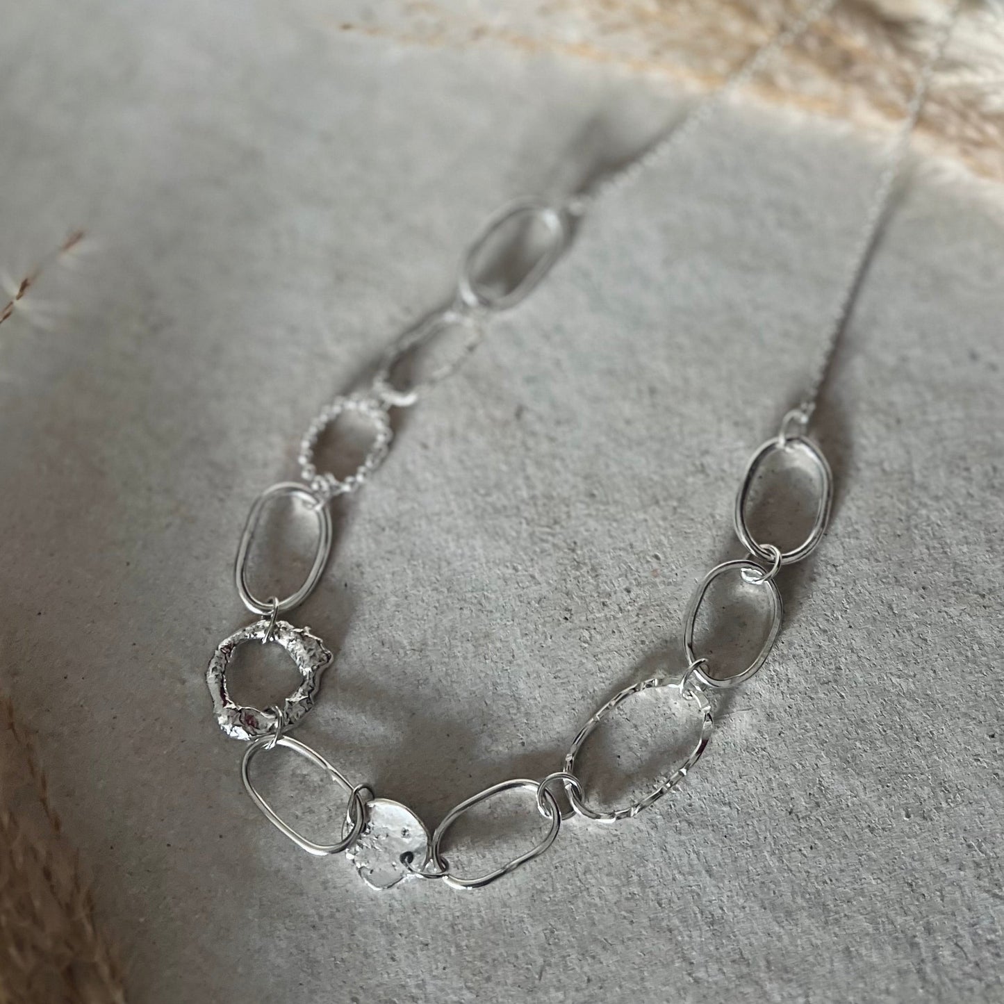 Silver necklace with irregularly shaped links on a textured surface