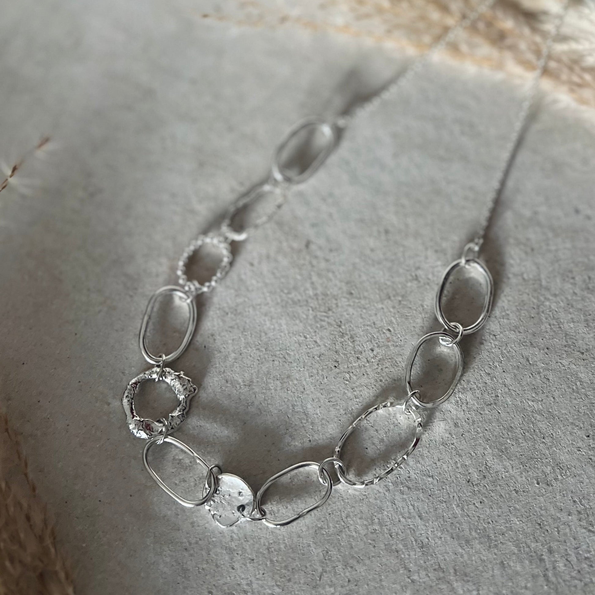 Silver necklace with irregularly shaped links on a textured surface