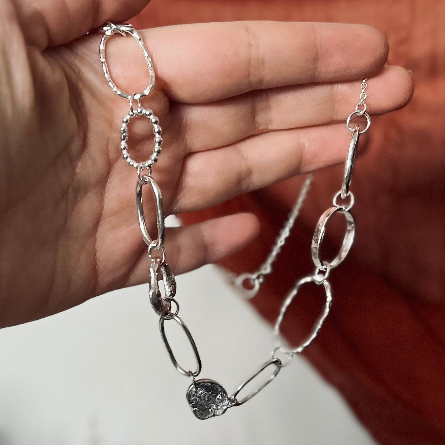 Silver chain bracelet with a heart-shaped clasp held by a hand against a blurred background