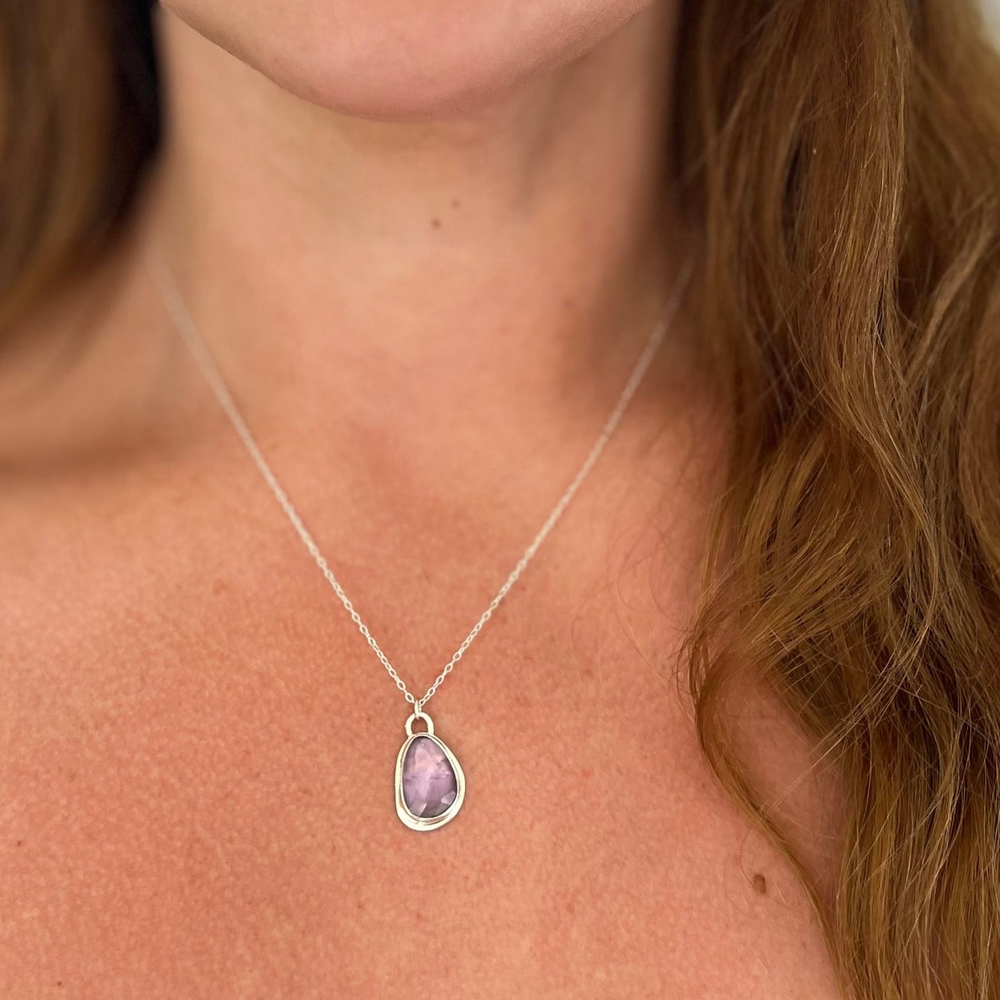 Necklace with a purple pendant worn by a person with long brown hair.