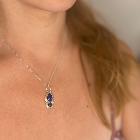Close-up of a necklace with blue and red stones on a pendant worn by a person
